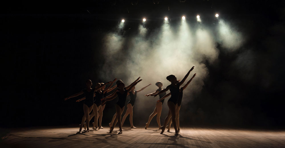 Ballet dancers on a school stage lit by theatre lights